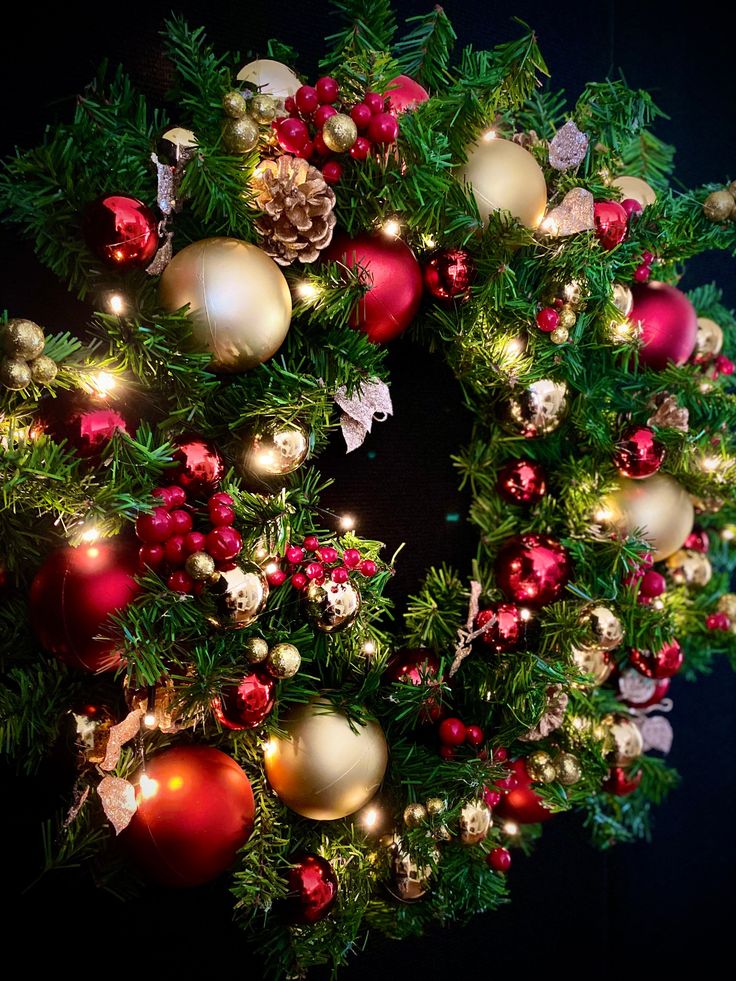 a christmas wreath with red and gold ornaments on the front, lit up by lights