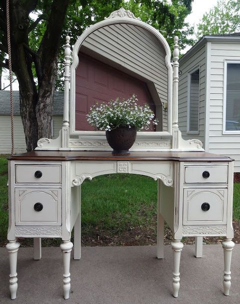 a white vanity with a mirror and flower pot on the top, sitting in front of a house