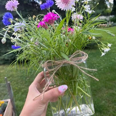 a person holding a vase filled with flowers in the middle of a yard, next to a lawn