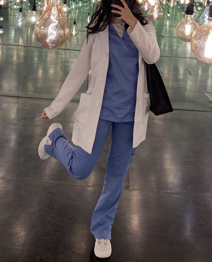 a woman in white jacket and blue pants dancing with lights hanging from the ceiling behind her