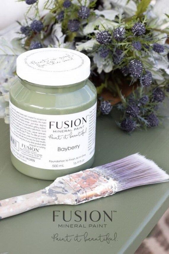 a green table with some flowers and a paintbrush on it next to the jar