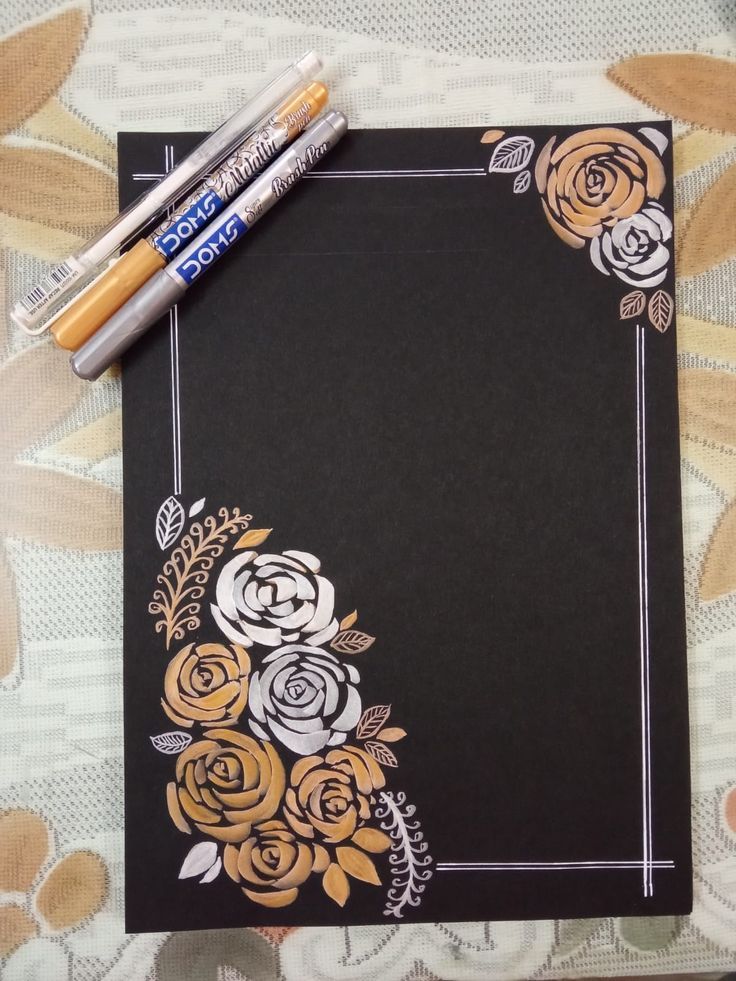 two pencils sitting on top of a black paper with gold and white flowers in it