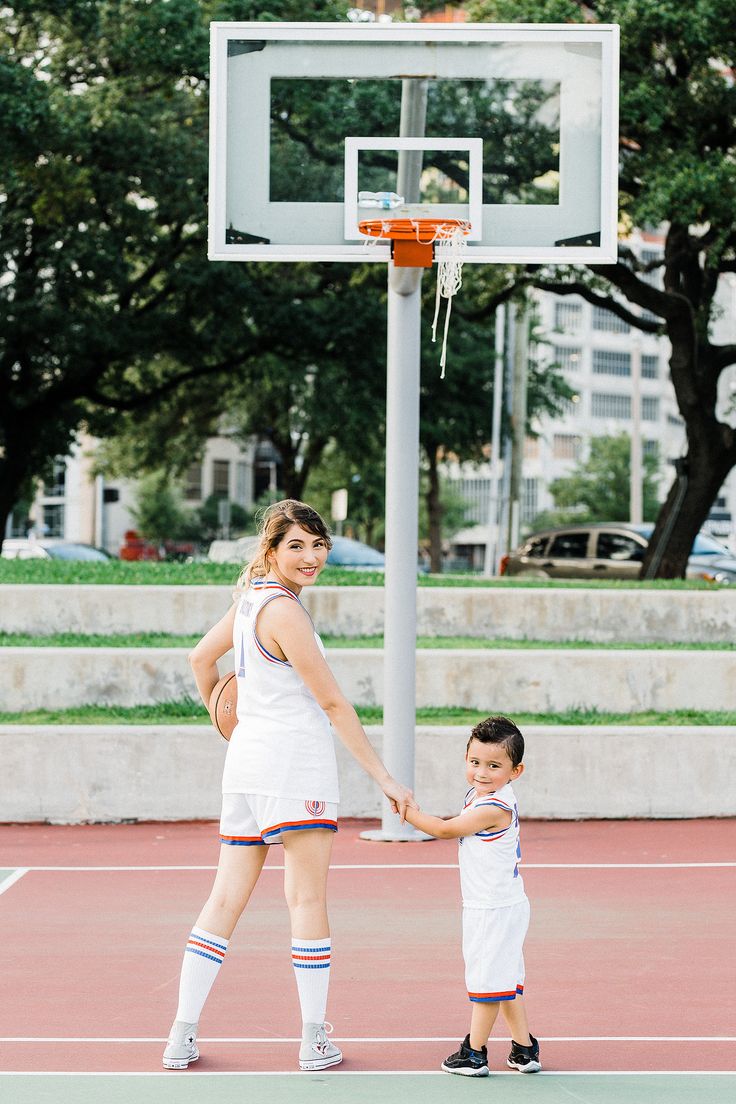 a woman holding the hand of a small boy on a basketball court with a basket