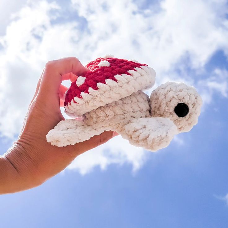 a hand holding a crocheted teddy bear in the sky