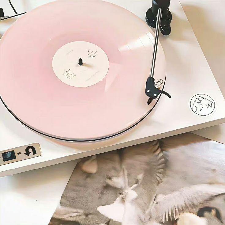 a pink record player sitting on top of a white table next to an album cover