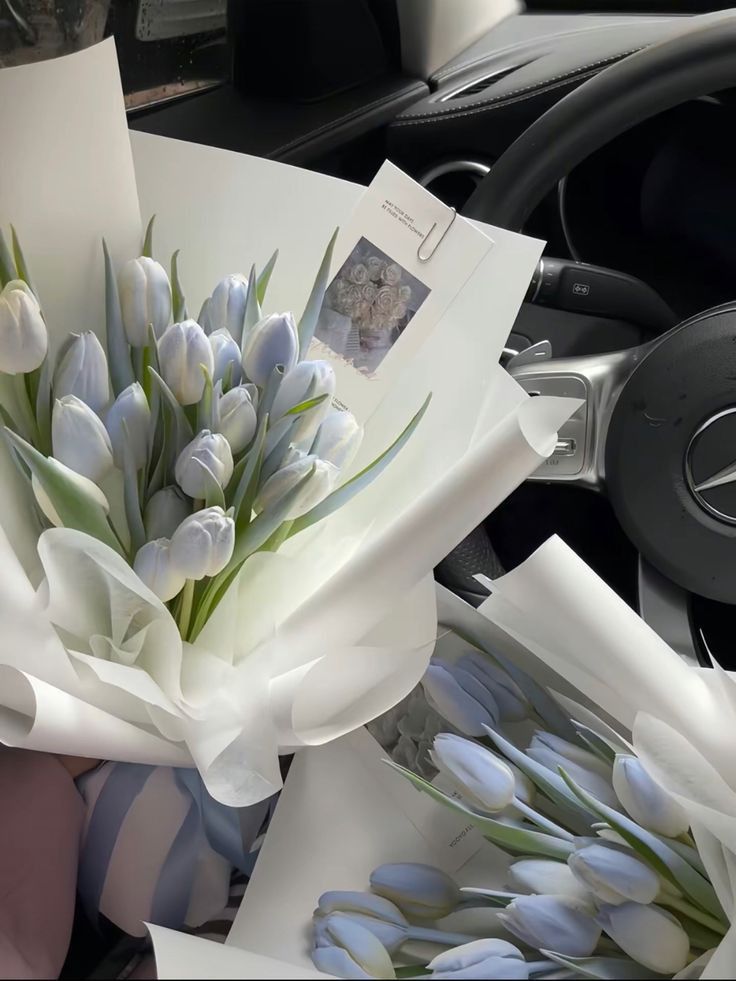 a bouquet of white tulips sitting on top of a table next to a car steering wheel