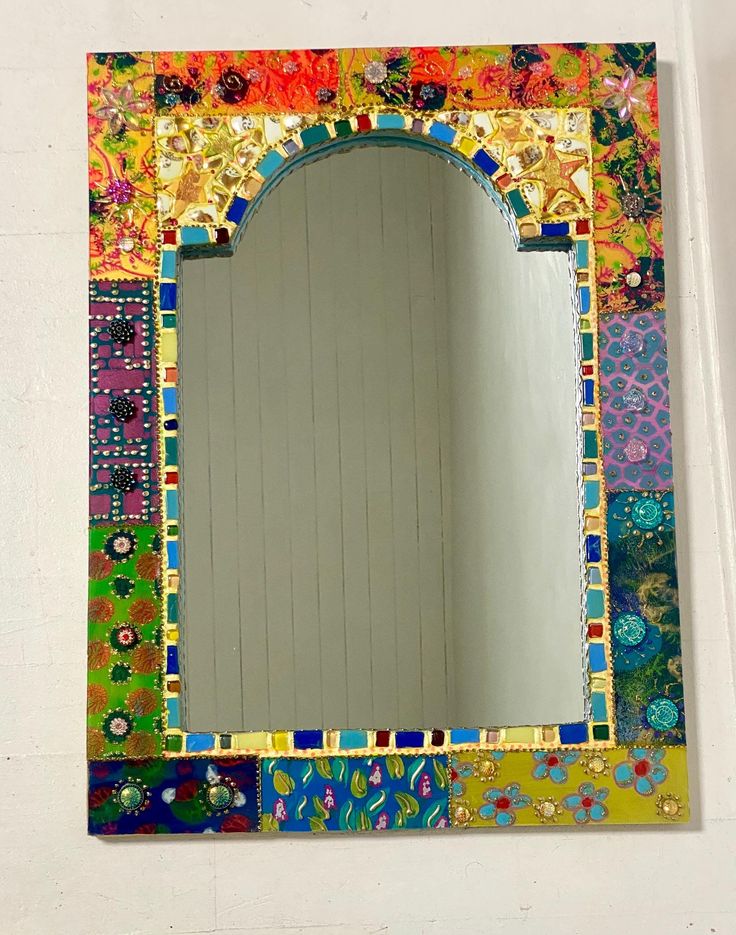 a mirror that has been decorated with colorful tiles and flowers on it, sitting against a white wall