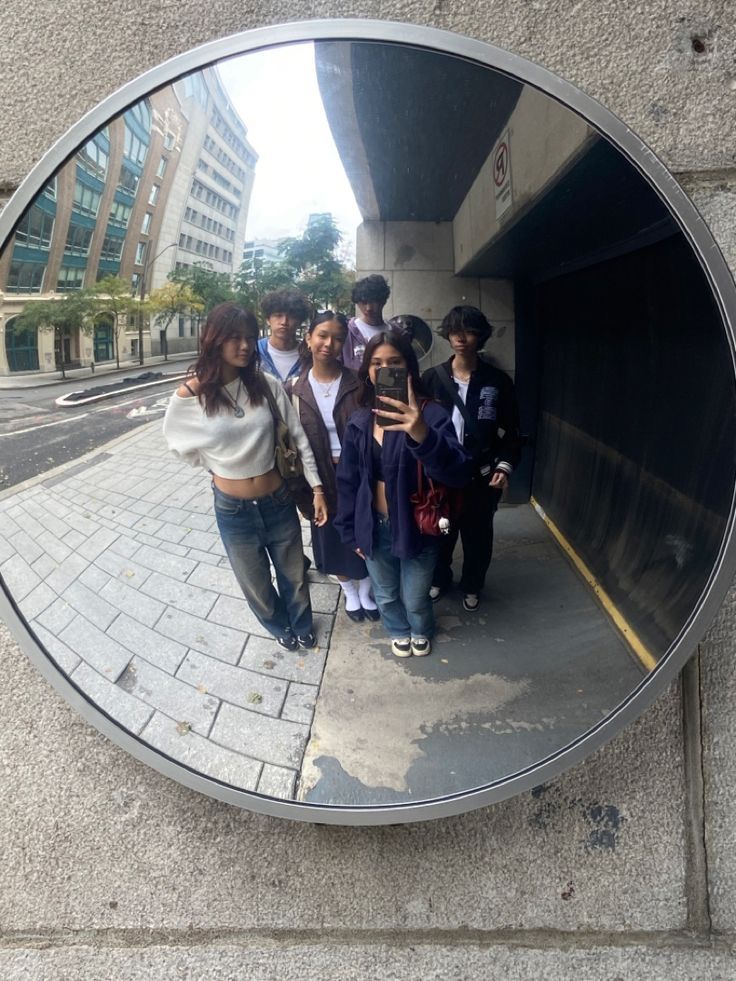 a group of young people standing in front of a round mirror on the side walk