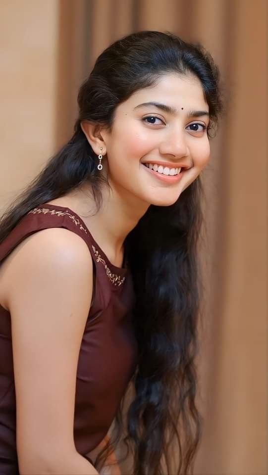 a woman with long black hair smiling at the camera while wearing a brown dress and earrings