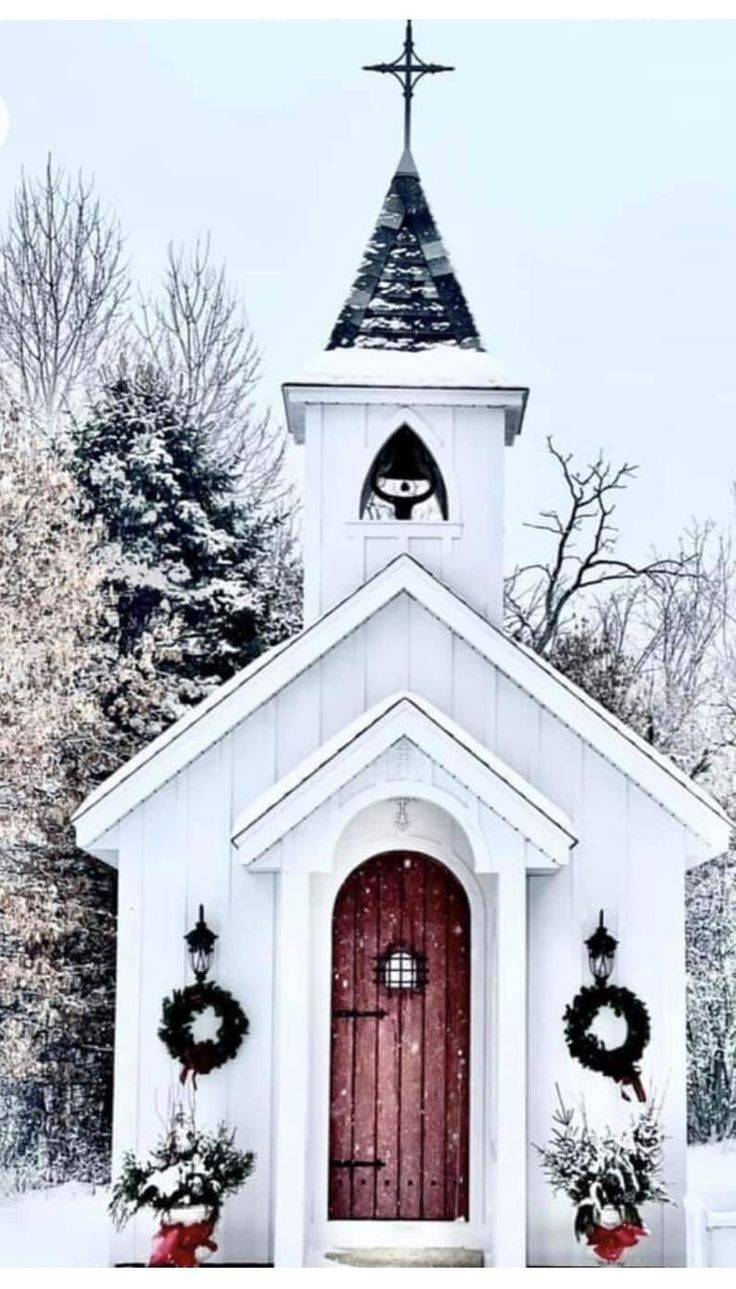 a small church with wreaths on the front door and steeple is covered in snow