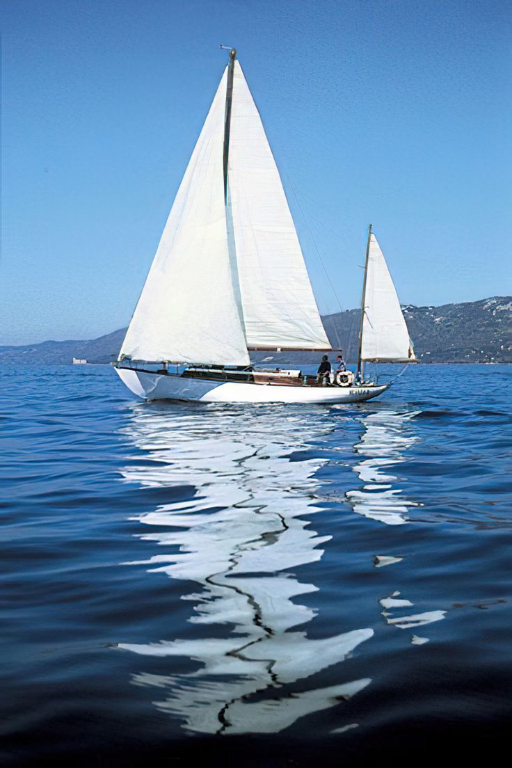 two sailboats are sailing in the ocean on a sunny day with blue skies and mountains behind them