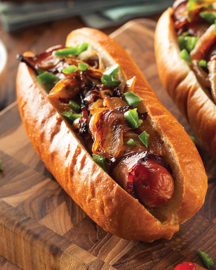 two hot dogs with toppings on a cutting board