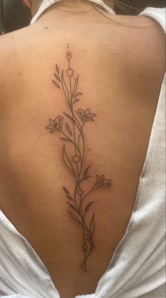 the back of a woman's shoulder with flowers and vines tattooed on her lower back