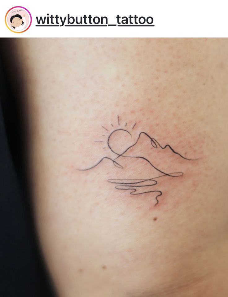 a small tattoo on the side of a woman's right arm, with mountains in the background