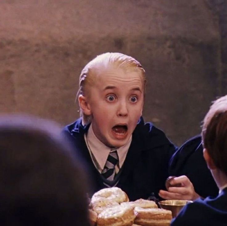 a young boy in a school uniform eating donuts with his mouth wide open and tongue out