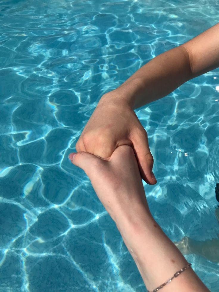 two people holding hands in the water near each other with their feet above the water