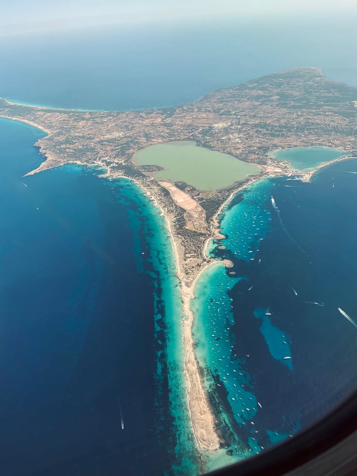 an aerial view of the ocean and land from inside an airplane window, looking down on some blue water