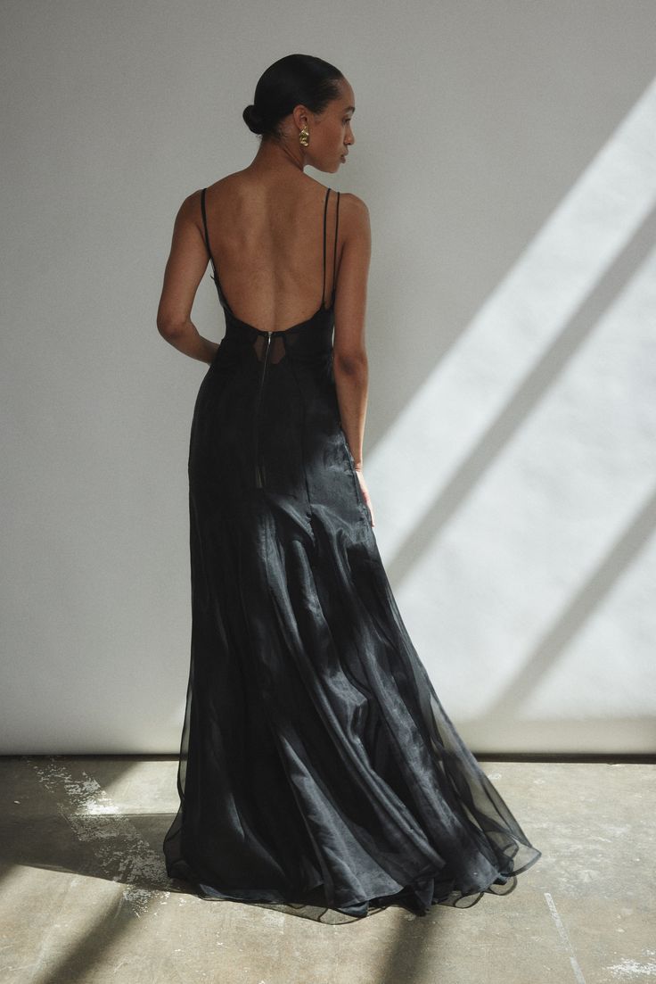 a woman in a long black dress standing against a white wall with her back to the camera