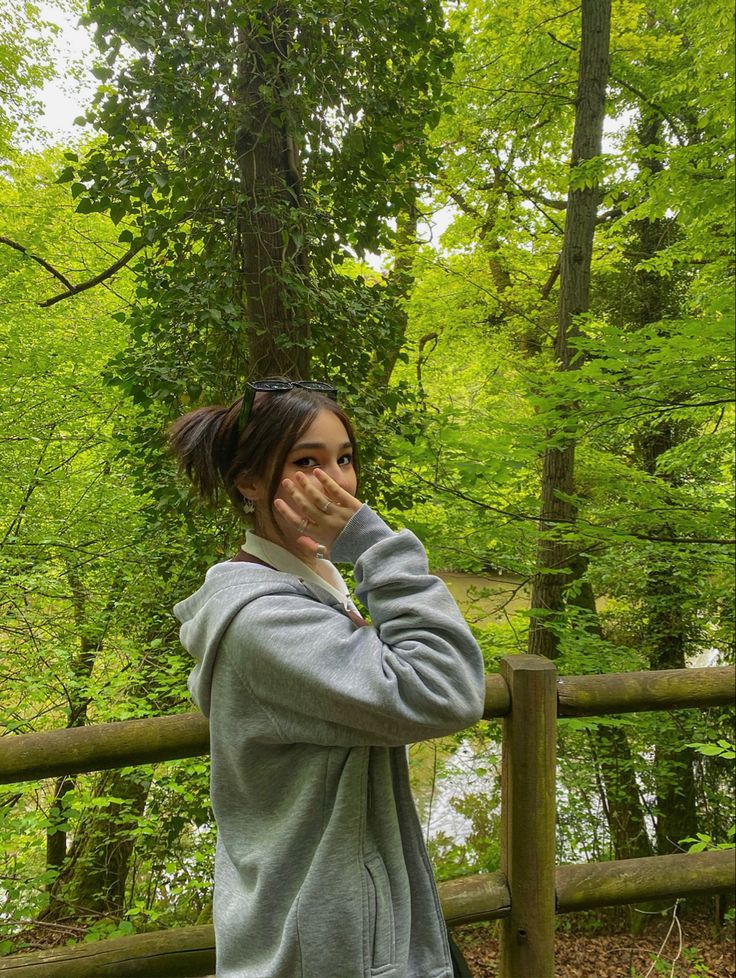 a woman standing in front of a fence talking on a cell phone while holding her hand up to her face