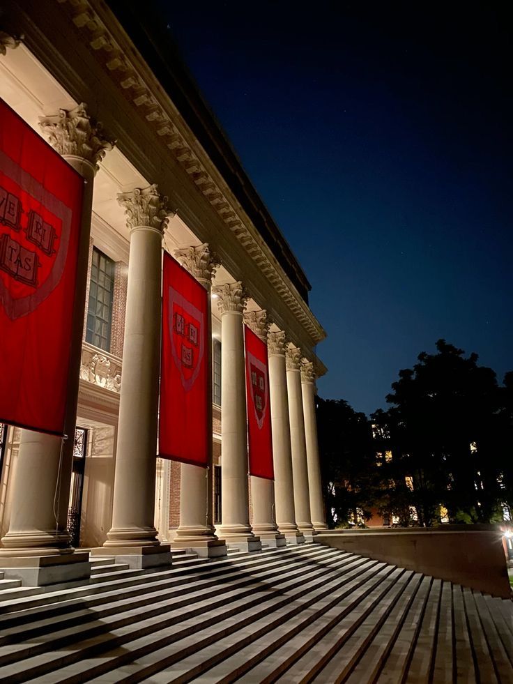 the building is lit up at night with red banners on it's pillars and steps