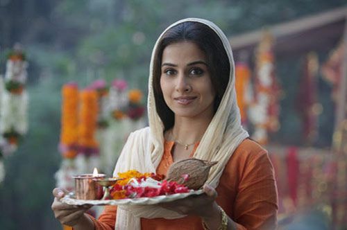 a woman holding a plate with food on it in front of flowers and candles behind her