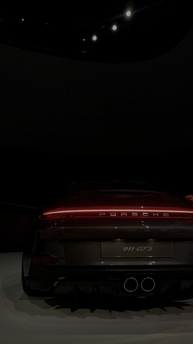 the back end of a red sports car in a dark room with spotlights on it