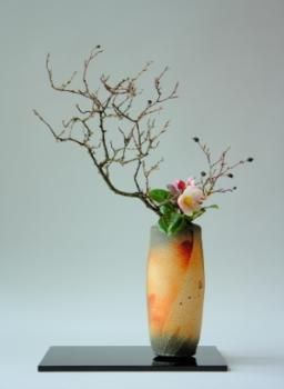 a vase with flowers in it sitting on a black stand against a white wall background