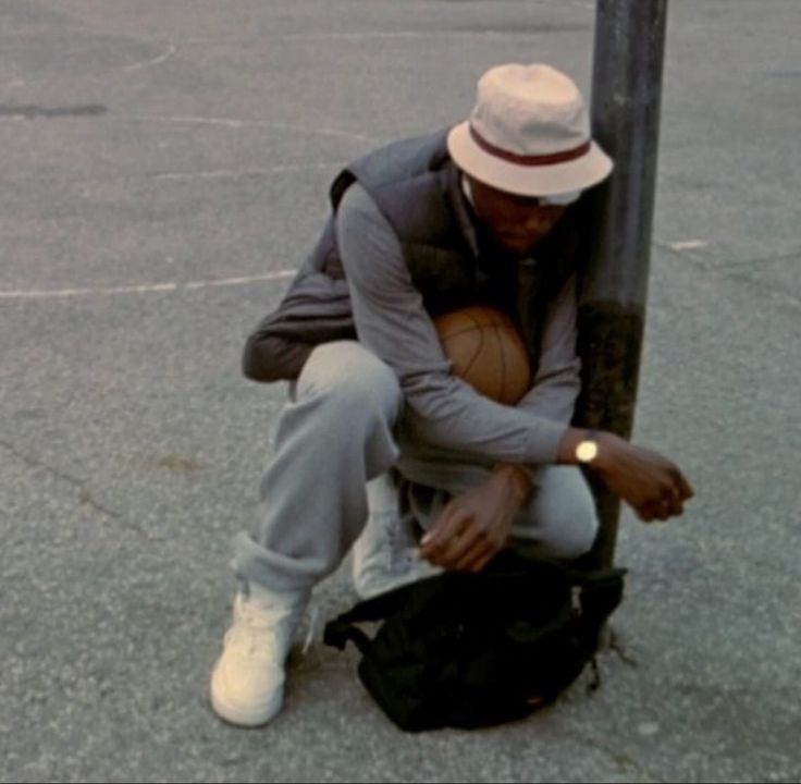 a man sitting on top of a bag next to a street pole holding a basketball