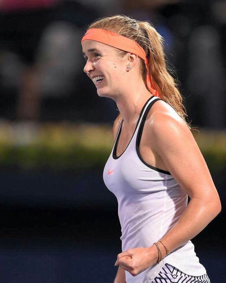 a female tennis player is smiling and holding her racquet in one hand while walking on the court