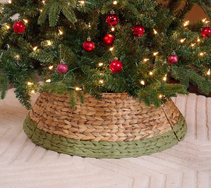 a small christmas tree in a woven basket with ornaments on it's top and lights around the base