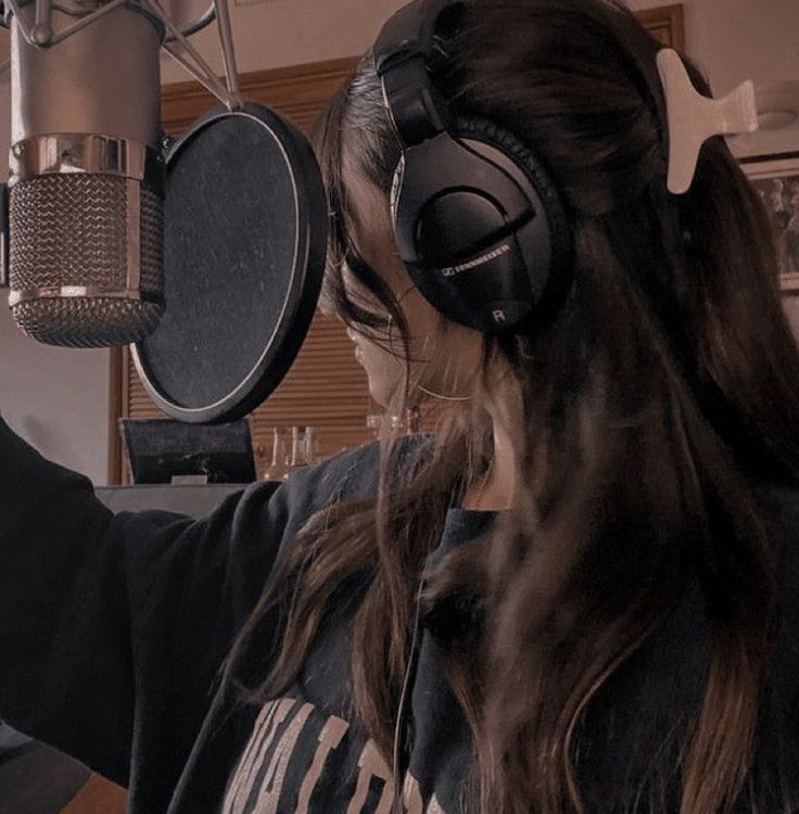 a woman wearing headphones is recording in front of a microphone