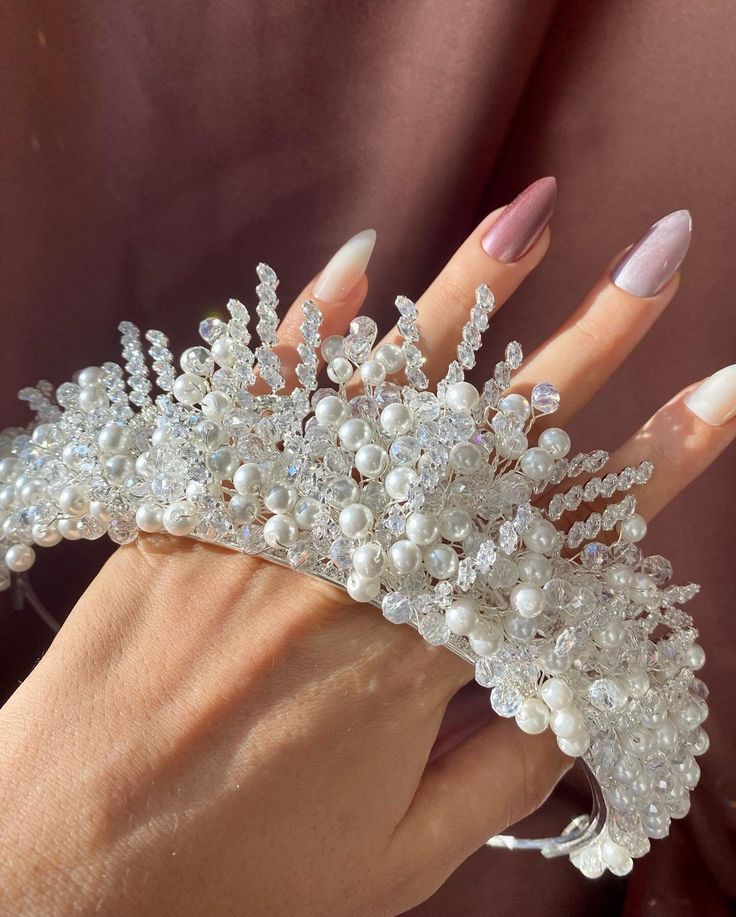 a woman's hand holding a wedding tiara with pearls and crystals on it