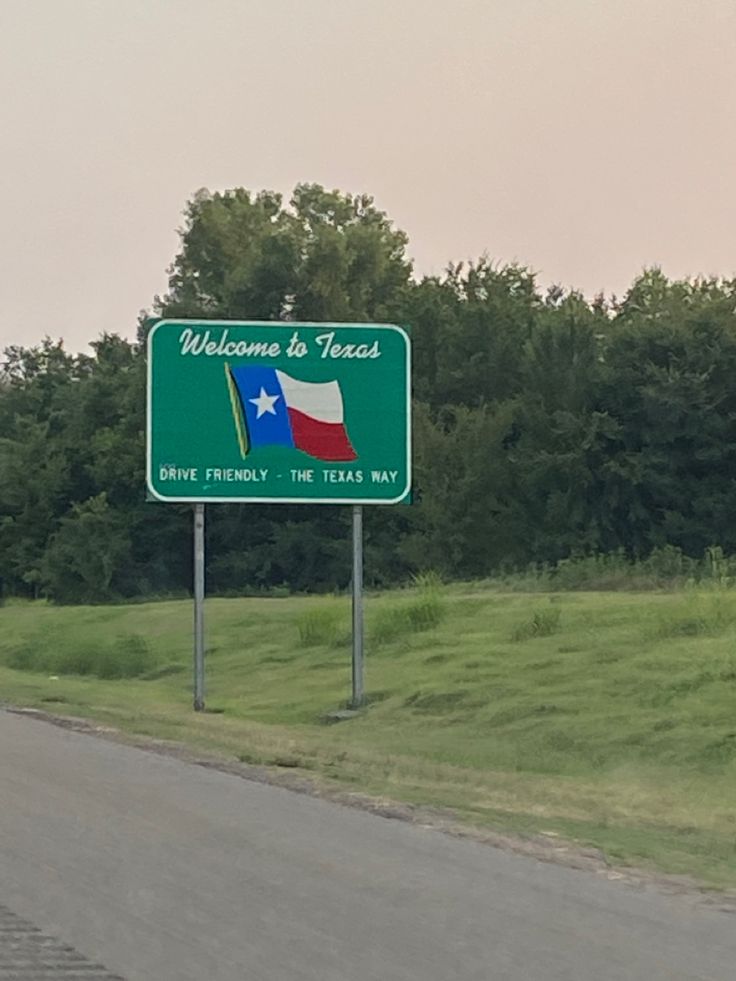 a welcome to texas sign on the side of a road with trees in the background