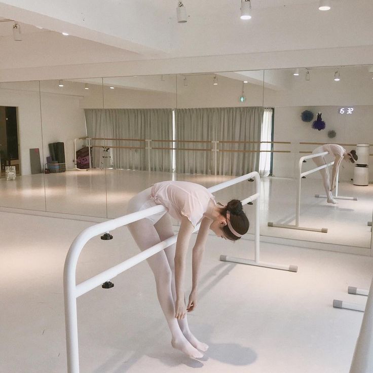 a ballerina is leaning over the rail in an empty room with mirrors on the walls