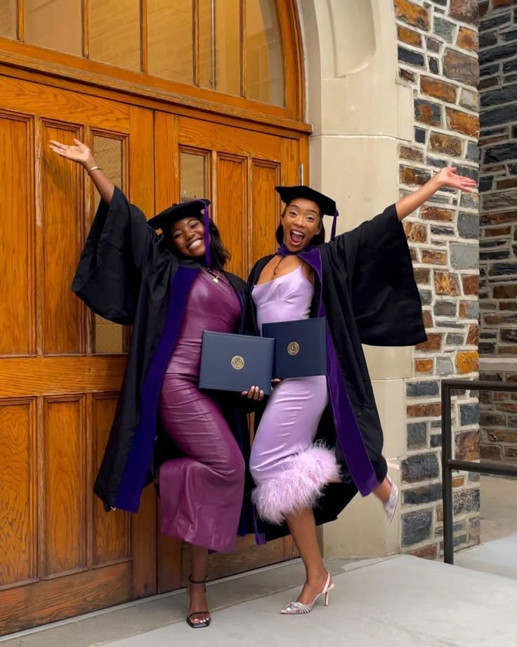 two women in graduation gowns are posing for a photo outside the doors of a church