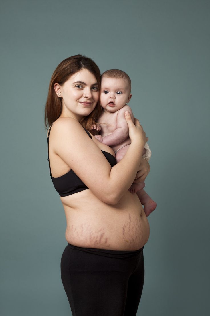 a woman holding a baby in her arms and smiling at the camera while standing against a gray background