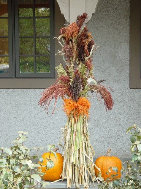 an arrangement of dried flowers and pumpkins in front of a house