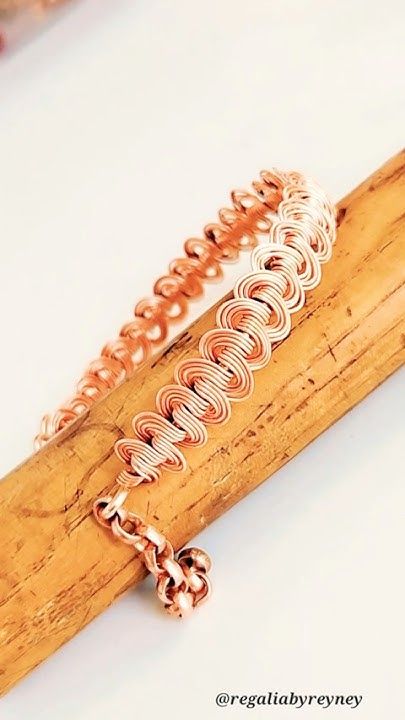 two bracelets are sitting on top of a piece of wood and one is made out of copper wire