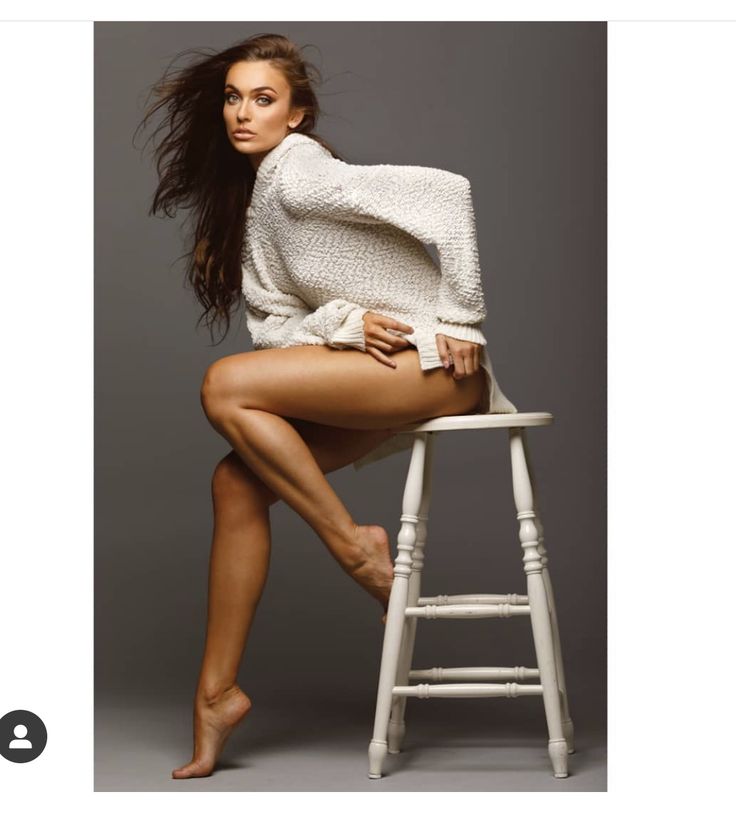 a woman sitting on top of a white stool next to a wooden chair with her legs crossed