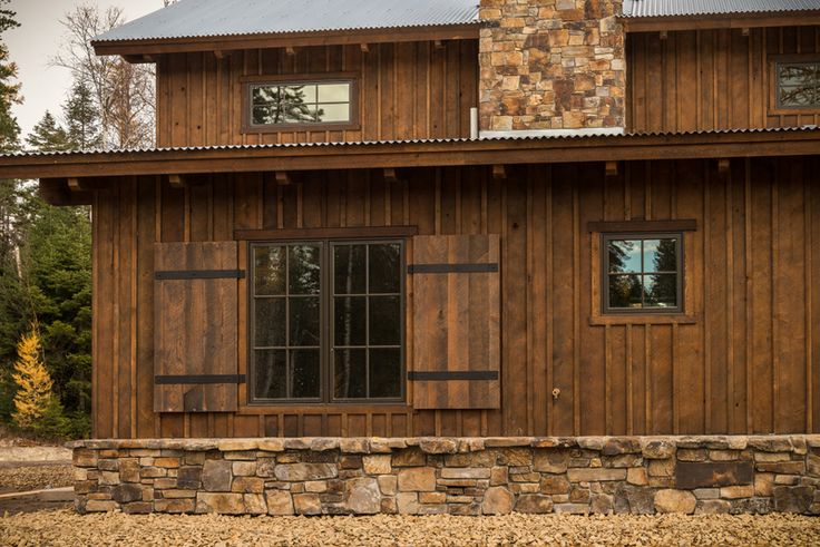 a wooden building with two windows and a stone wall