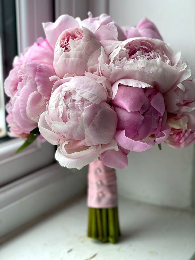 a bouquet of pink peonies in front of a window