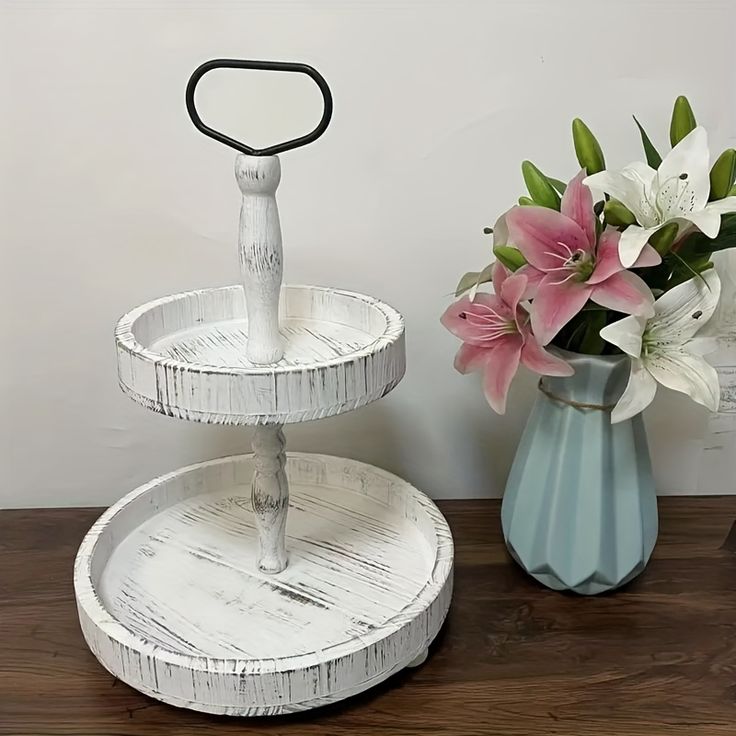 two tiered trays with flowers in them on a wooden table next to a vase