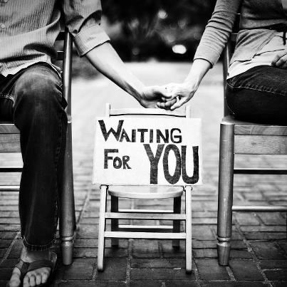 two people sitting on chairs holding hands with a waiting for you sign in front of them