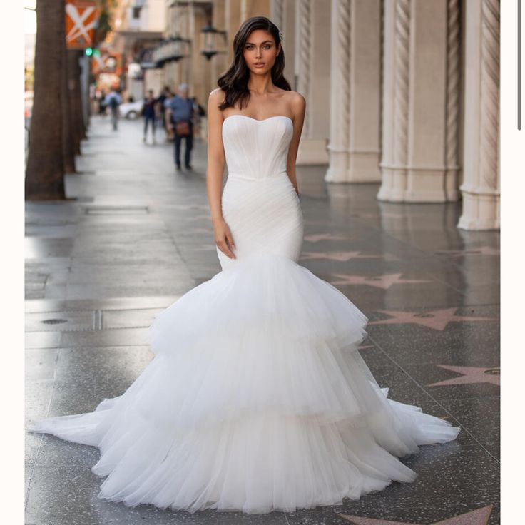 a woman in a white wedding dress standing on the sidewalk