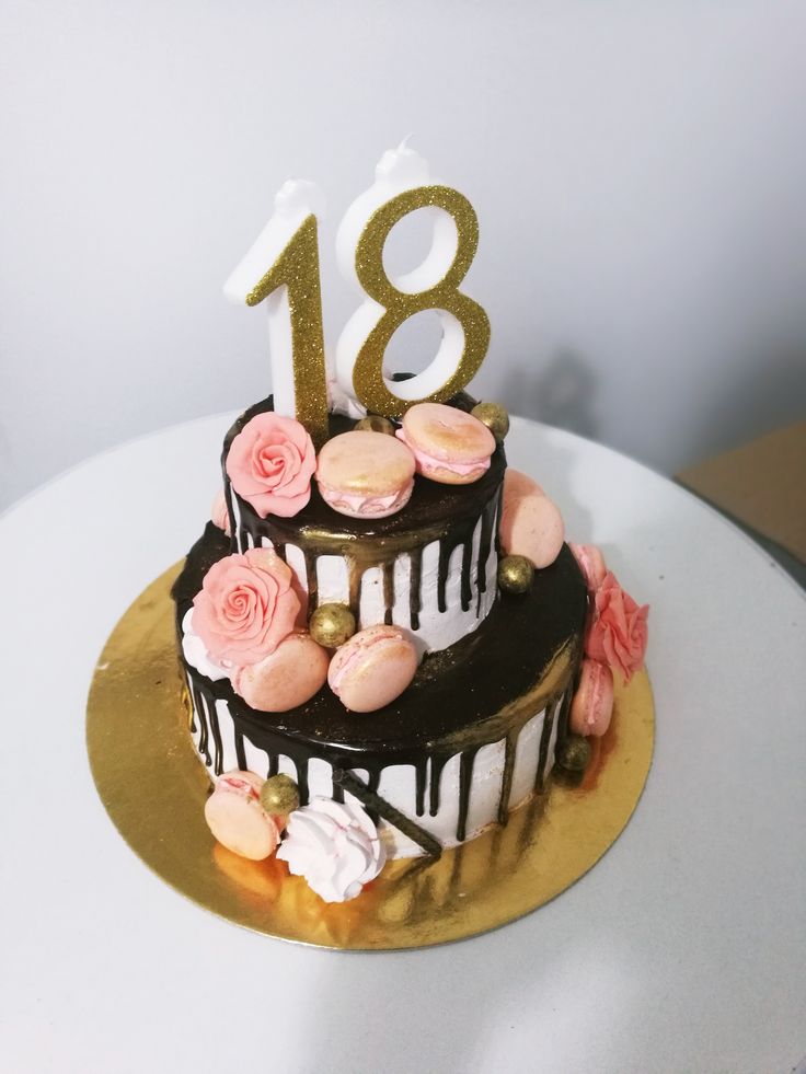 a three tiered chocolate cake with pink flowers and gold numbers on the top, sitting on a white table