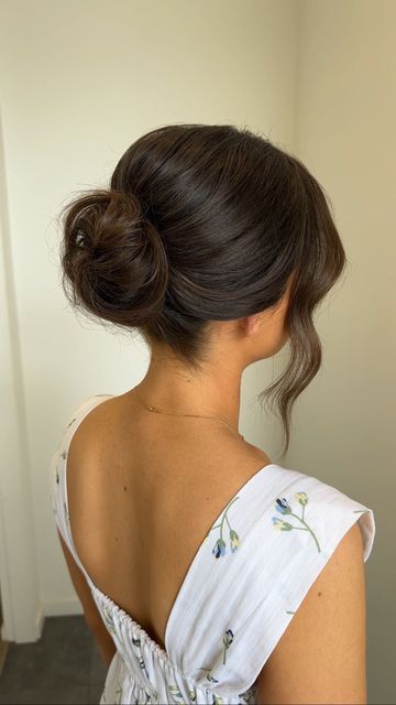 a woman in a white dress with her back turned to the camera, wearing a messy bun