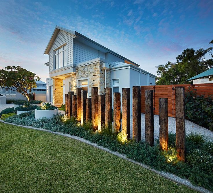 a modern house with wooden posts and lights on the front yard at dusk, in australia