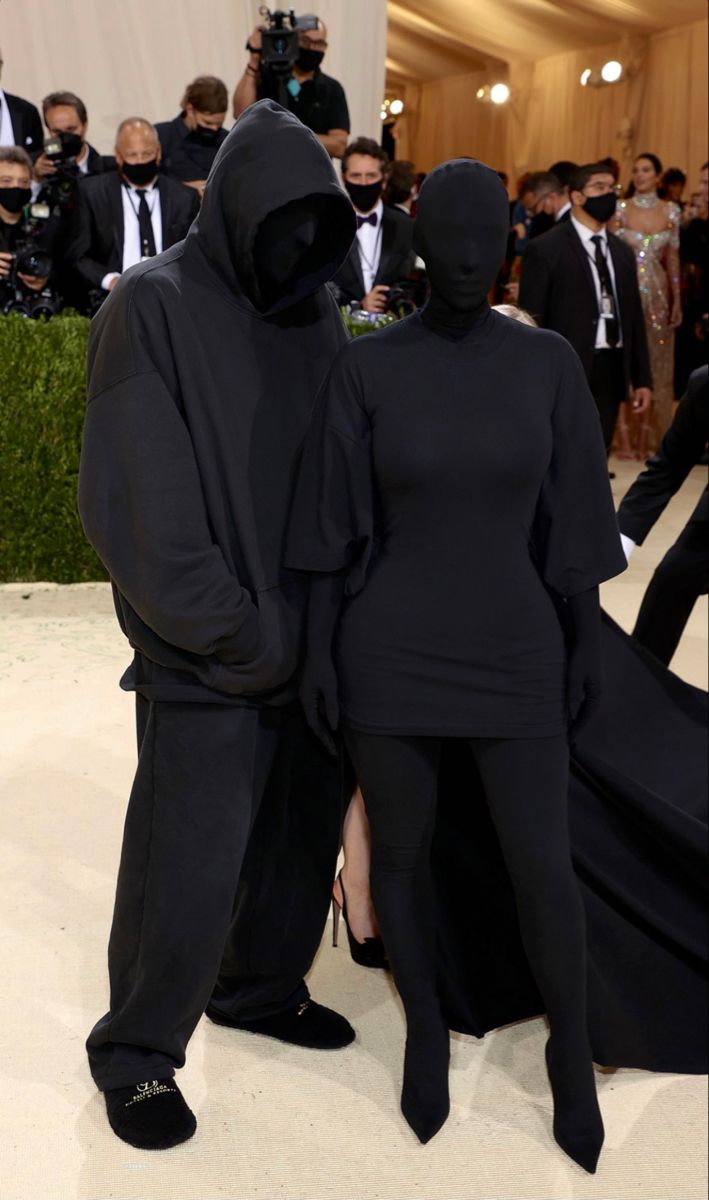 two people in black outfits standing next to each other at an event with cameras around them