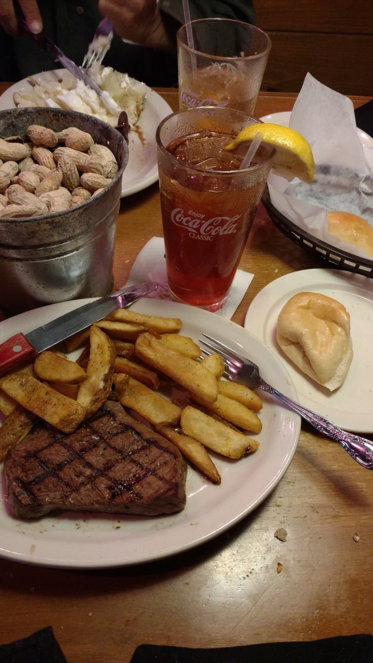 steak, french fries and soda are sitting on the table with other food items in front of them