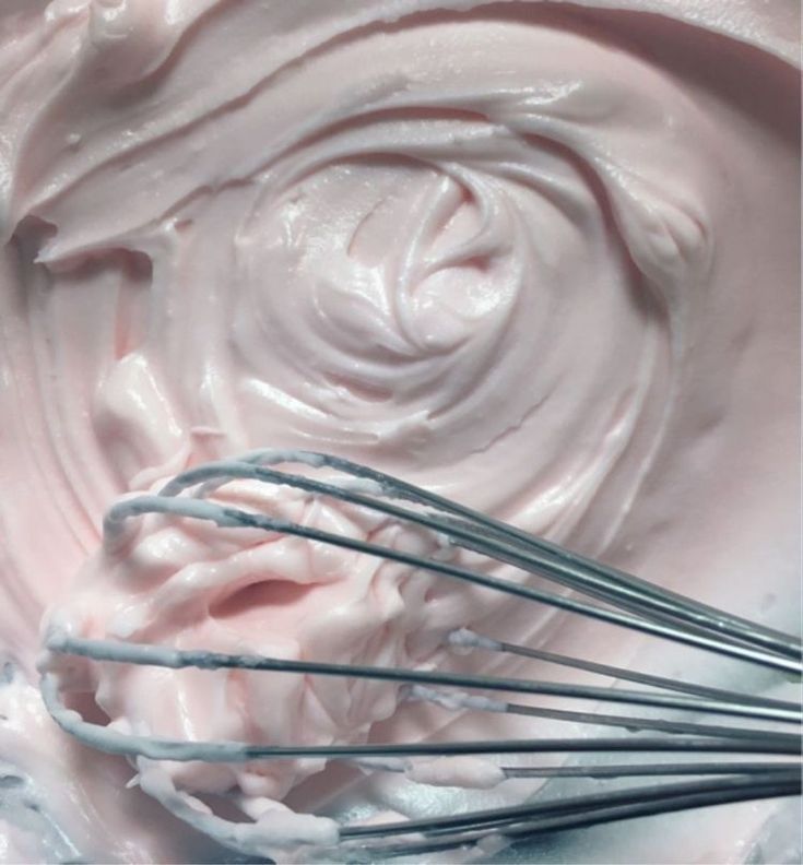 a whisk in a mixing bowl filled with pink whipped cream and other ingredients